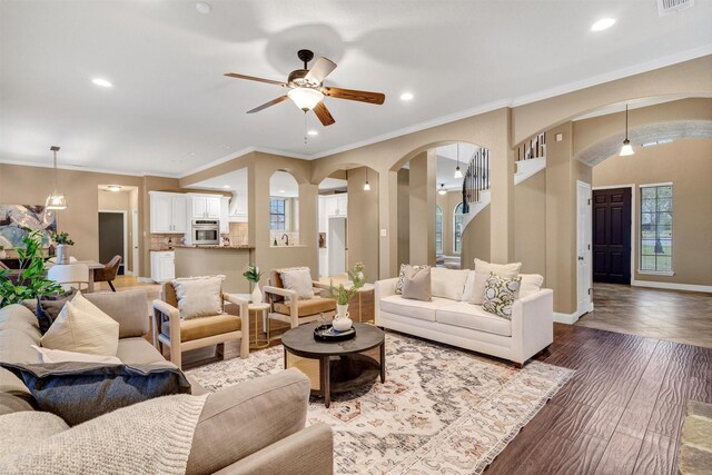 living room featuring arched walkways, baseboards, recessed lighting, a ceiling fan, and crown molding