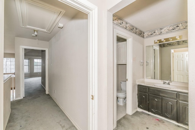 hallway featuring attic access, a sink, and baseboards