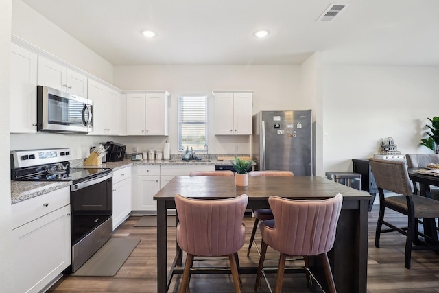 13420 Hiskey Dr, Fort Worth, TX 76052 - kitchen with appliances with stainless steel finishes, dark wood-type flooring, recessed lighting, white cabinetry, and a kitchen breakfast bar