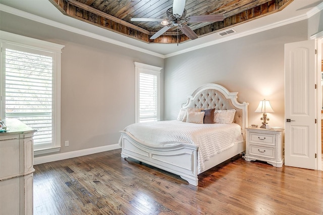 bedroom with a raised ceiling, wood finished floors, multiple windows, and visible vents