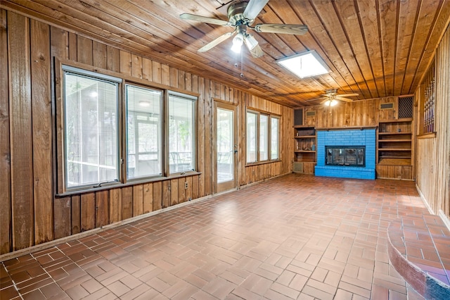 302 Comanche Dr, Gainesville, TX 76240 - unfurnished living room featuring wooden walls, a ceiling fan, wood ceiling, a skylight, and brick floor