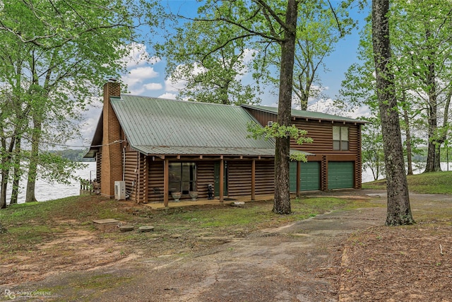 view of front of home with log siding, a chimney, driveway, a garage, and metal roof