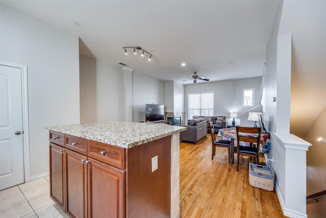13900 Noel Rd Unit 16, Dallas, TX 75240 - kitchen featuring ceiling fan, light countertops, brown cabinetry, a center island, and light wood-style flooring
