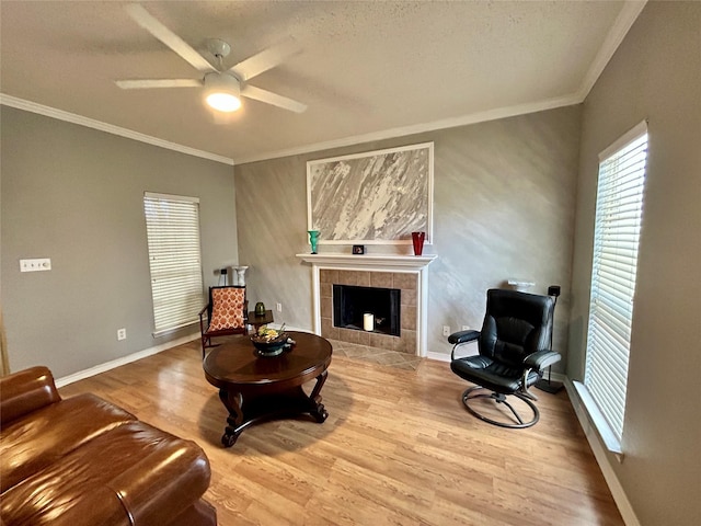 sitting room with ornamental molding, baseboards, ceiling fan, a tiled fireplace, and wood finished floors