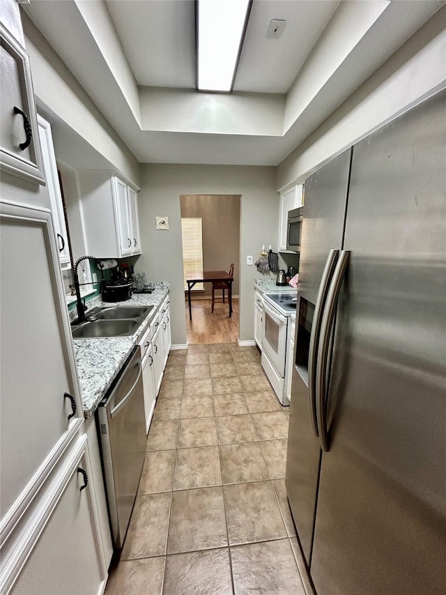 kitchen with a sink, white cabinetry, light tile patterned floors, baseboards, and stainless steel appliances