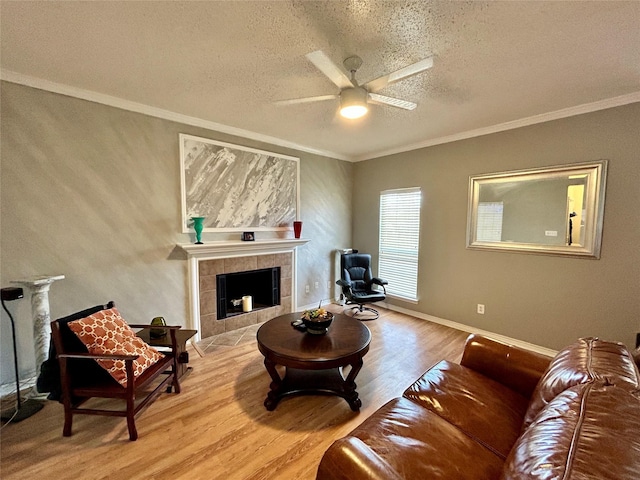 living room with a tile fireplace, a ceiling fan, a textured ceiling, light wood-style flooring, and ornamental molding