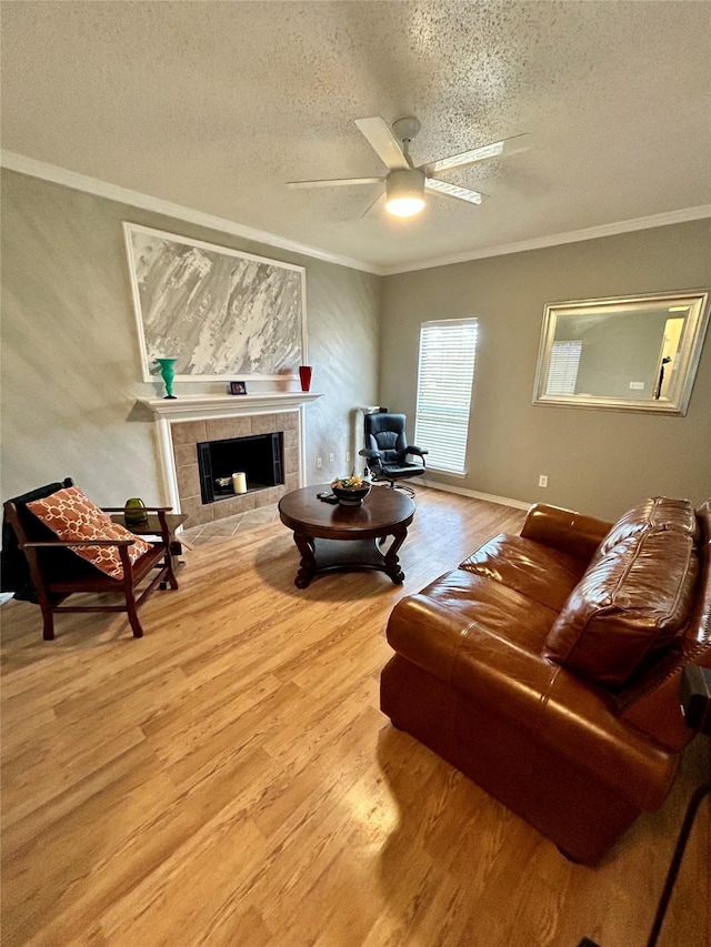 living area featuring a textured ceiling, crown molding, wood finished floors, a tiled fireplace, and a ceiling fan