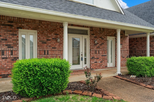 entrance to property featuring a porch, brick siding, and roof with shingles