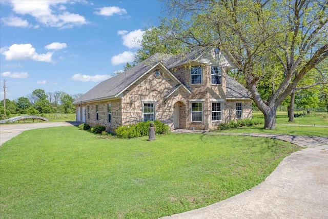 view of front facade featuring driveway, stone siding, and a front lawn
