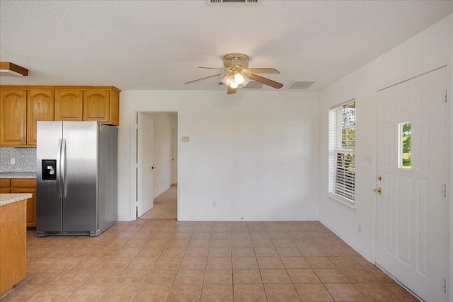 kitchen with visible vents, ceiling fan, stainless steel fridge with ice dispenser, brown cabinetry, and light countertops