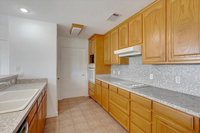 kitchen with a sink, visible vents, white appliances, under cabinet range hood, and light tile patterned floors