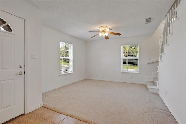 foyer entrance with visible vents, ceiling fan, plenty of natural light, and light carpet
