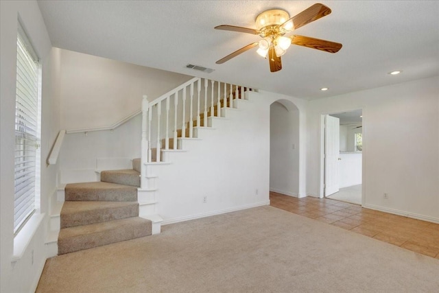 interior space featuring tile patterned floors, ceiling fan, arched walkways, carpet flooring, and visible vents