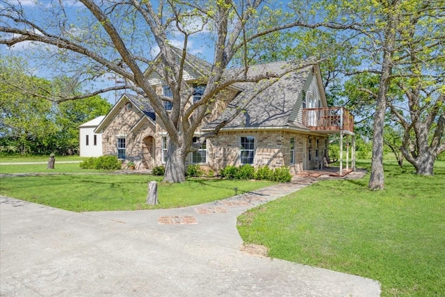 traditional-style house featuring a balcony, a front yard, and stone siding