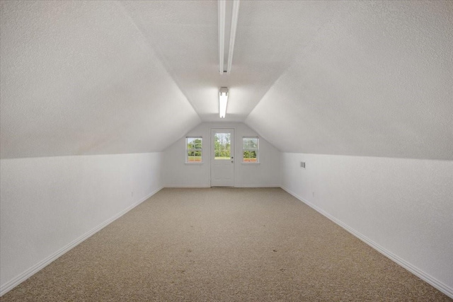 bonus room featuring a textured ceiling, light carpet, lofted ceiling, and baseboards