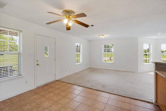foyer entrance with a healthy amount of sunlight, a ceiling fan, light colored carpet, and light tile patterned floors