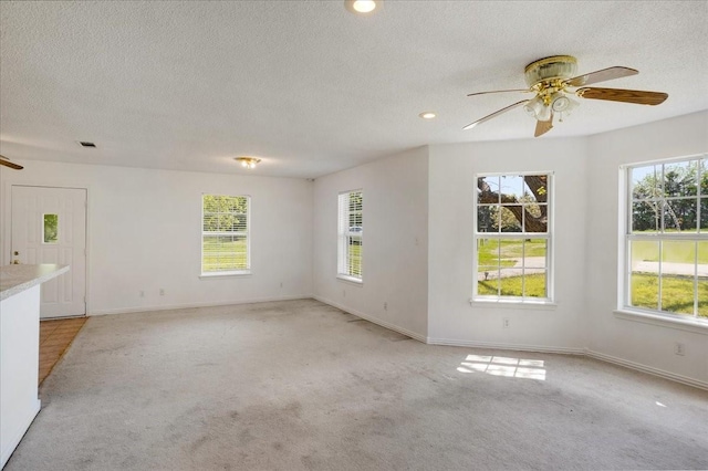 unfurnished room with baseboards, a textured ceiling, a ceiling fan, and light colored carpet