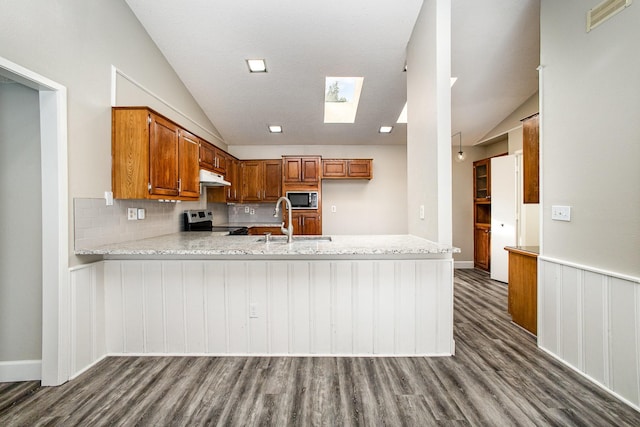 kitchen with brown cabinets, under cabinet range hood, lofted ceiling with skylight, and stainless steel electric range