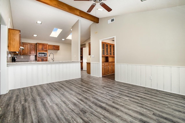 unfurnished living room featuring a sink, wainscoting, visible vents, a ceiling fan, and wood finished floors