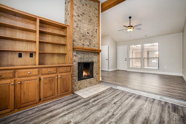 unfurnished living room with wood finished floors, a brick fireplace, a ceiling fan, and baseboards