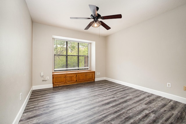 empty room featuring dark wood-type flooring, a ceiling fan, and baseboards
