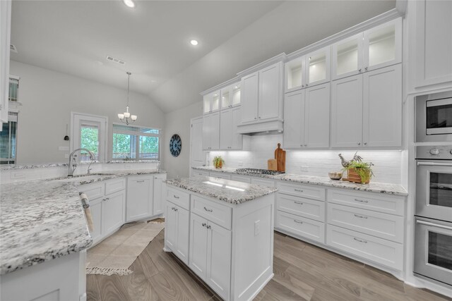 kitchen featuring vaulted ceiling, a sink, decorative backsplash, appliances with stainless steel finishes, and visible vents