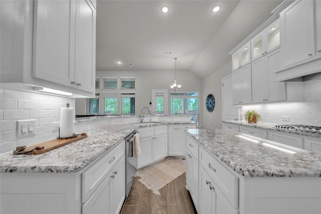 kitchen featuring lofted ceiling, stainless steel appliances, a sink, a peninsula, and white cabinetry