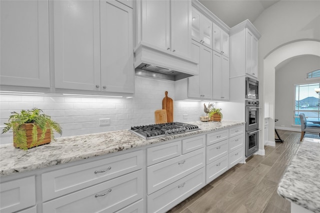 kitchen featuring white cabinets, light wood finished floors, arched walkways, decorative backsplash, and appliances with stainless steel finishes