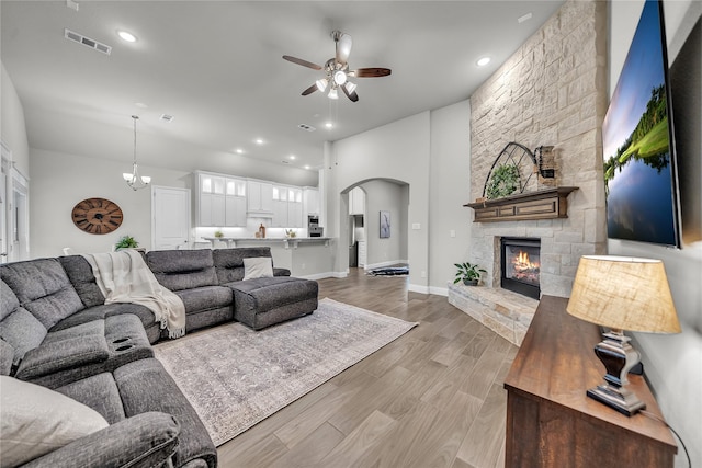 living room featuring a ceiling fan, a stone fireplace, arched walkways, light wood finished floors, and visible vents