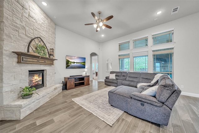 living room featuring visible vents, arched walkways, baseboards, a fireplace, and ceiling fan