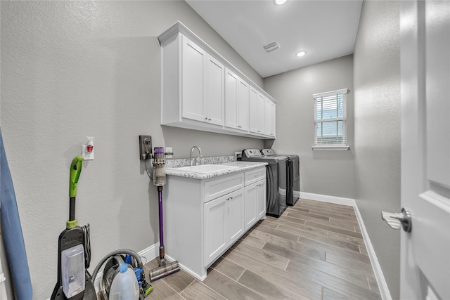 laundry area with washing machine and clothes dryer, a sink, light wood-type flooring, baseboards, and cabinet space