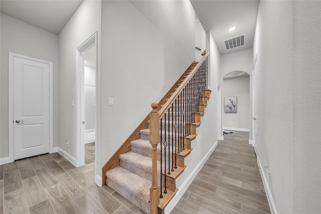 stairs featuring arched walkways, wood finished floors, visible vents, and baseboards