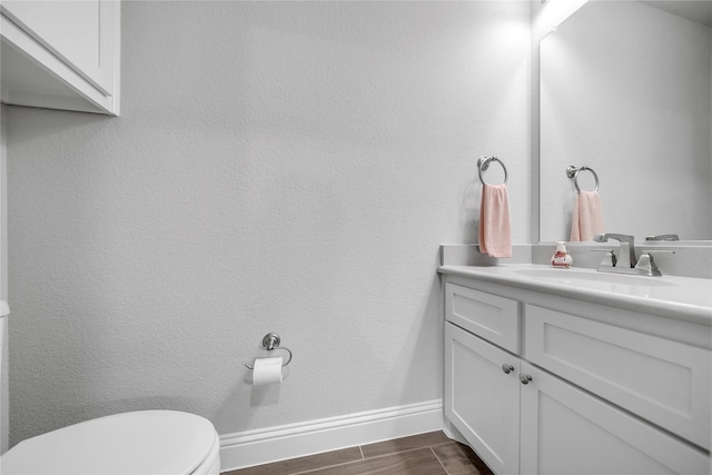 half bathroom featuring baseboards, wood finished floors, toilet, and vanity