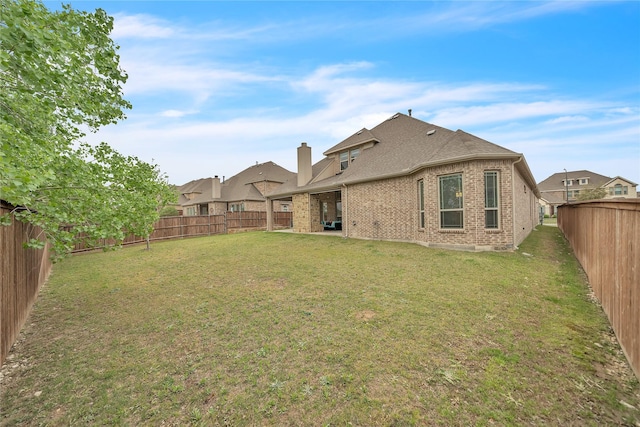 back of property with roof with shingles, a fenced backyard, a chimney, brick siding, and a lawn