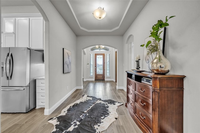 foyer entrance with baseboards, arched walkways, a notable chandelier, and a raised ceiling