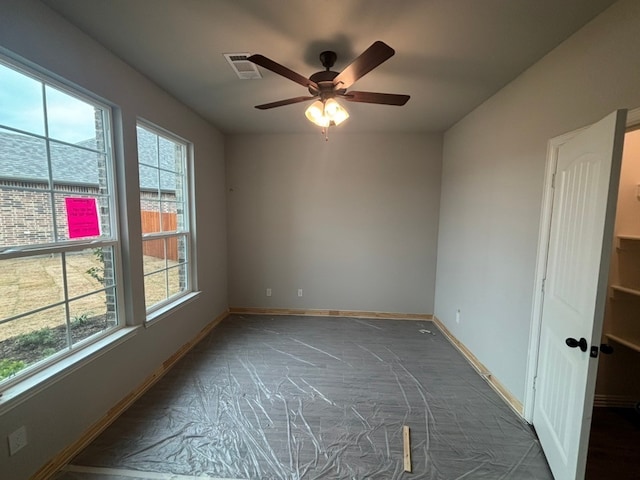 unfurnished room with a ceiling fan, visible vents, dark carpet, and plenty of natural light