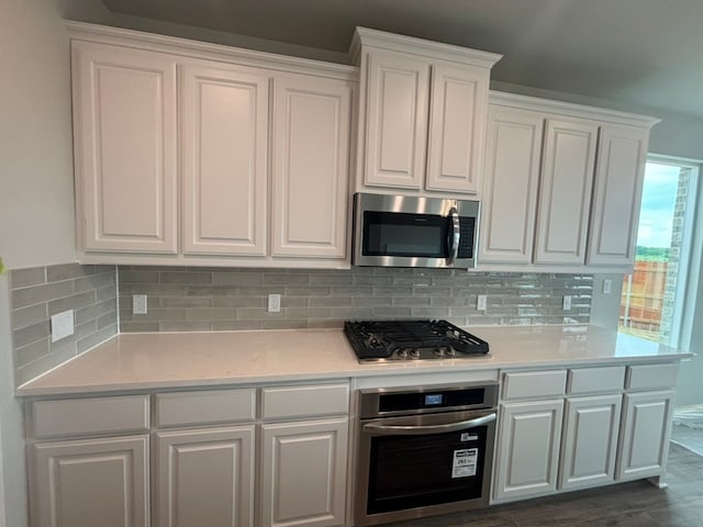 kitchen with white cabinets, appliances with stainless steel finishes, light countertops, dark wood-style floors, and backsplash