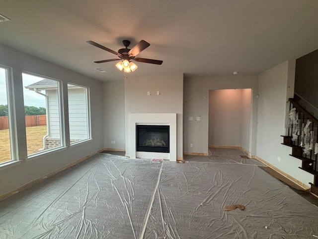 unfurnished living room featuring stairway, visible vents, baseboards, a glass covered fireplace, and a ceiling fan