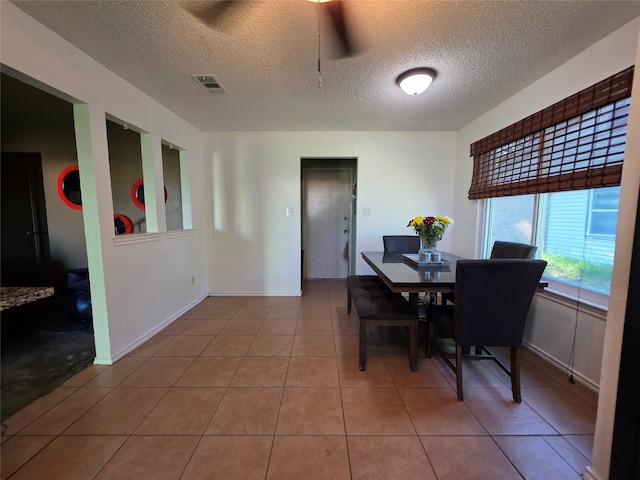 tiled dining room featuring baseboards, visible vents, and a textured ceiling