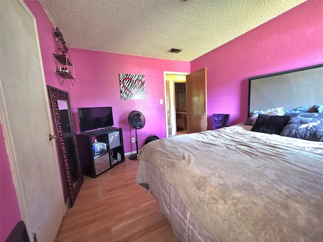 bedroom featuring a textured wall, visible vents, a textured ceiling, and wood finished floors