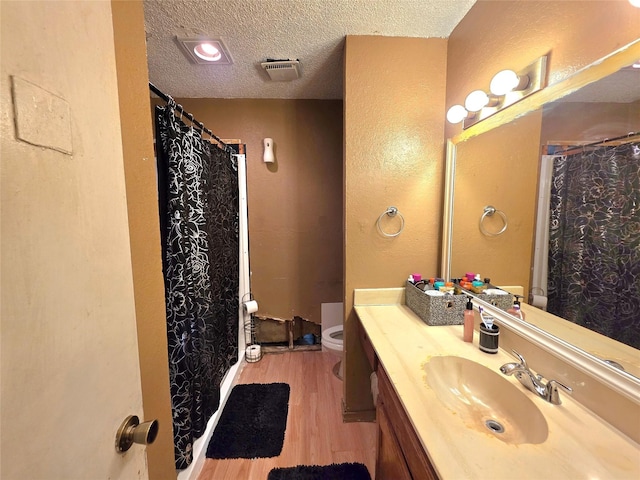 full bathroom with toilet, wood finished floors, vanity, a textured ceiling, and visible vents