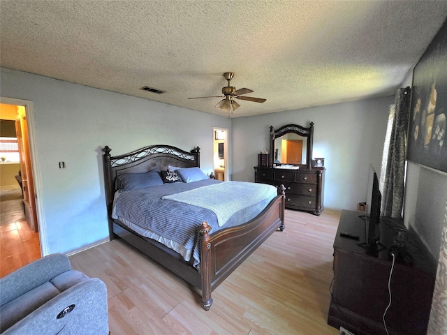 bedroom with a textured ceiling, visible vents, light wood-style flooring, and a ceiling fan