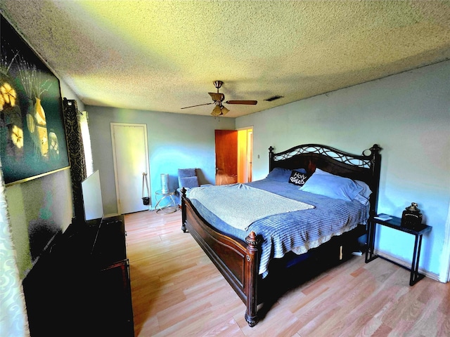 bedroom featuring light wood-type flooring, visible vents, a ceiling fan, and a textured ceiling