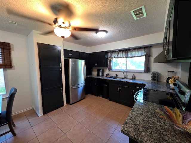 kitchen with a sink, a textured ceiling, visible vents, dark cabinets, and appliances with stainless steel finishes
