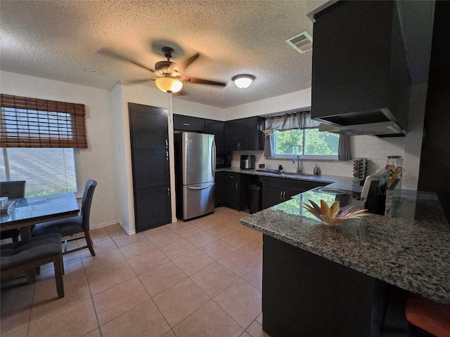 kitchen with freestanding refrigerator, dark stone counters, a textured ceiling, visible vents, and dark cabinetry