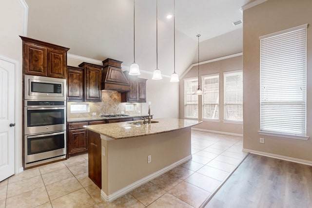 kitchen with custom exhaust hood, a sink, appliances with stainless steel finishes, an island with sink, and vaulted ceiling