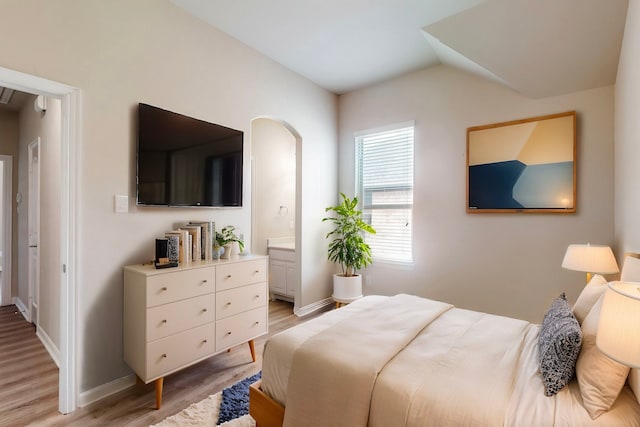 bedroom featuring arched walkways, light wood-style flooring, baseboards, and lofted ceiling