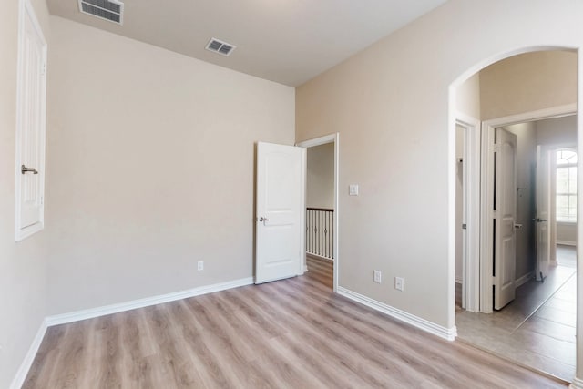 unfurnished bedroom featuring visible vents, baseboards, light wood finished floors, and arched walkways