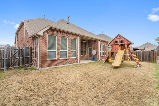rear view of property with brick siding, a fenced backyard, a playground, and a lawn