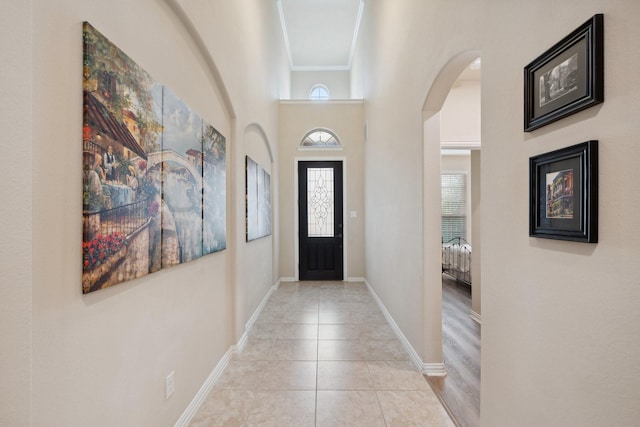 foyer with arched walkways, light tile patterned floors, baseboards, and ornamental molding